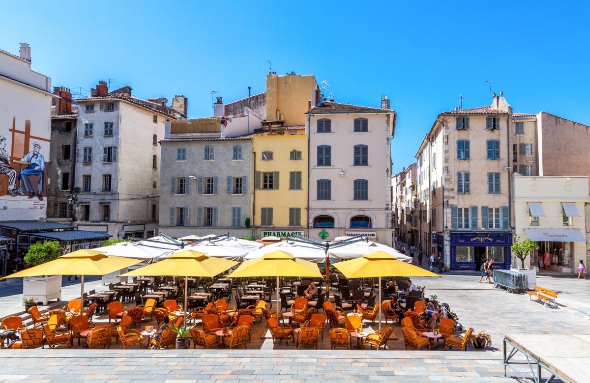 Terrasse de café avec chaises orange et parasols jaunes sur une place ensoleillée