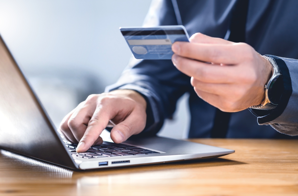 Mains saisissant une carte bancaire devant un ordinateur portable pour un paiement en ligne