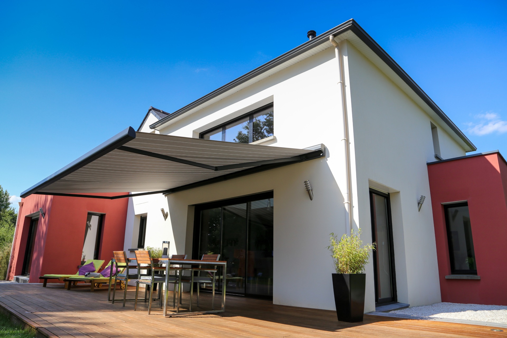 Maison moderne avec store banne déployé sur une terrasse en bois ensoleillée